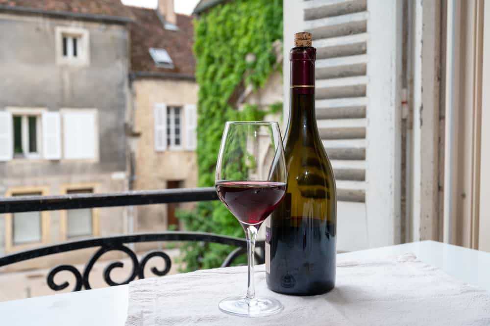 Bourgogne rødvin i glas og flaske med udsigt til hyggelig fransk landsby i baggrunden.