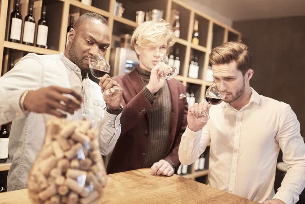Tre unge mænd der dufter og smager på vin til et vinsmagningsarrangement.